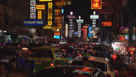 Busy-cityscape-clip-at-nighttime-in-Chinatown,-Bangkok,-showing-lines-of-traffic,-bright-neon-signs,-and-crowds-of-people