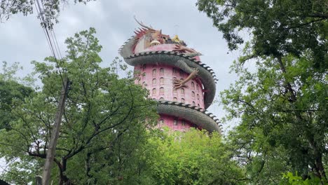 Tilt-up-view-of-the-unique-and-impressive-Wat-Samphran-that-features-a-17-story,-bright-pink-tower-with-a-dragon-coiling-around-it-in-Nakhon-Pathom-province,-West-of-Bangkok,-Thailand