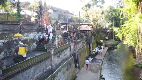 Panorama-Aéreo-De-Los-Balineses-Rezando-En-El-Antiguo-Templo-Del-Bosque-En-Bali-Indonesia,-Antigua-Arquitectura-Samuan-Tiga-Y-Vegetación-Bajo-La-Luz-Del-Sol