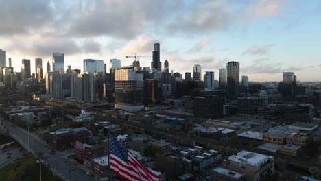 Aerial-view-risng-over-the-US-Flag,-toward-the-downtown-Chicago,-during-sunrise