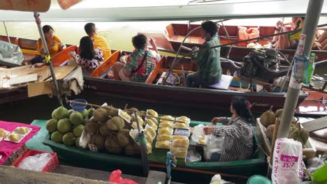Tourists-enjoy-the-boat-ride,-and-vendors-sell-fresh-fruits-from-their-boats-in-Damnoen-Saduak-Floating-Market,-the-vibrant-scenery-in-Ratchaburi-province,-South-West-of-Bangkok,-Thailand