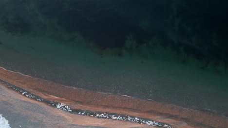 Drone-shot-looking-straight-down-on-a-beach-in-the-spring-when-there-is-still-some-snow-on-the-ground