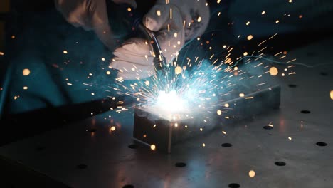 Close-up-welder-wearing-protective-mask-working-on-metal-with-a-welding-machine,-sparks-and-flashes,-super-slow-motion