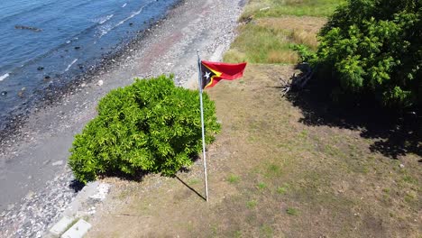 Aerial-drone-view-of-national-flag-of-Timor-Leste-along-the-shoreline-of-tropical-Atauro-Island-in-East-Timor,-Southeast-Asia