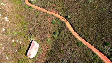 A-drone-view-of-people-hiking-on-a-dirt-road-on-the-side-of-a-steep-hill