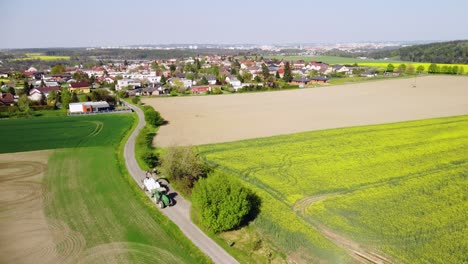 Scenery-view-of-vast-field-with-furrows-located-near-village-houses-under-hill-in-daylight-in-countryside