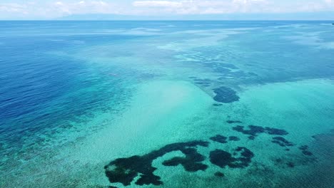 Seascape-aerial-view-flying-over-crystal-clear-turquoise-ocean-water-with-stunning-coral-reef-in-Timor-Leste,-Southeast-Asia