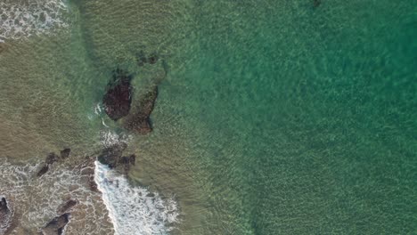 Top-view-shot-of-green-water-waves-rolling-onto-rocks