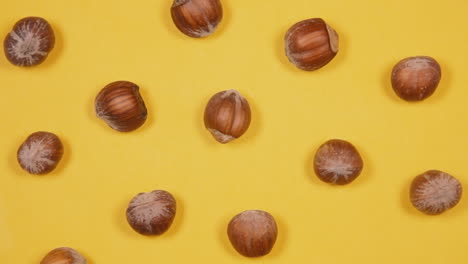 A-delightful-showing-of-healthy-brown-hazelnuts,-arranged-in-a-geometric-pattern,-rotating-over-a-yellow-background