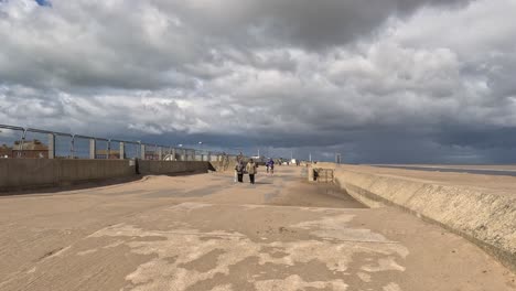 Wohltätigkeitsläufer-Laufen-Entlang-Einer-Strandpromenade-Neben-Einem-Sandstrand-Mit-Grauen-Gewitterwolken-Und-Strahlendem-Sonnenschein