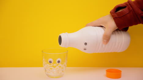 Pouring-milk-from-a-white-plastic-bottle-with-googly-eyes-into-a-glass-with-the-same-funny-face