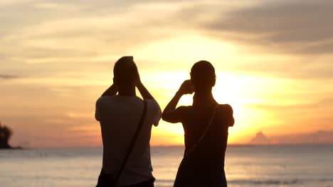 Ein-Paar-Fotografiert-Den-Sonnenuntergang-Per-Smartphone-Am-Strand