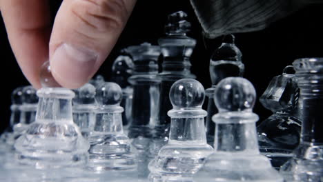 The-hand-of-a-player-carefully-picking-a-glass-pawn-from-a-chessboard-,-in-order-to-make-the-first-move-of-the-match