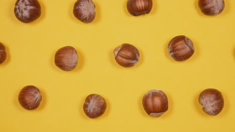 A-captivating-presentation-of-healthy-brown-hazelnuts,-arranged-in-a-geometric-pattern,-rotating-over-a-yellow-background
