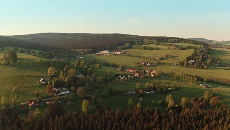 Drone-shot-of-czech-highlands-village-surrounded-with-forest-during-sunset