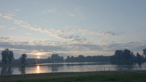 Vogel-Fliegt-über-Einem-See-Vorbei,-Während-Die-Frühe-Morgensonne-Aufgeht