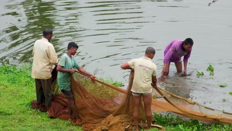 Un-Grupo-De-Pescadores-Reuniéndose-Y-Colocando-Sus-Redes-De-Pesca-En-La-Hierba-Con-El-Río-Al-Fondo