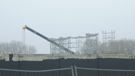 Intensive-work-on-the-construction-site-located-near-the-coast-of-the-sea,-mobile-crane-moving,-overcast-day-with-fog,-distant-wide-shot