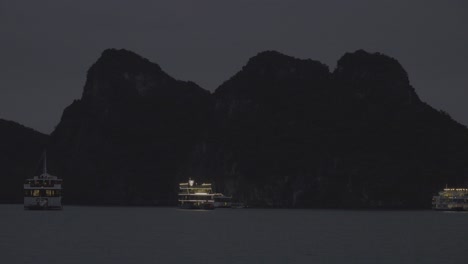 Un-Barco-Turístico-Iluminado-Con-El-Telón-De-Fondo-De-Una-Montaña-En-La-Bahía-De-Ha-Long,-Vietnam,-Por-La-Noche