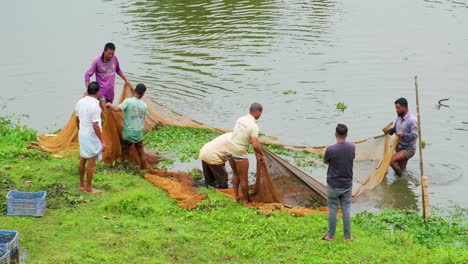 Eine-Gruppe-Von-Fischern-Versammelt-Sich-Und-Stellt-Ihre-Fischernetze-Auf-Dem-Gras-Auf,-Mit-Dem-Fluss-Im-Hintergrund