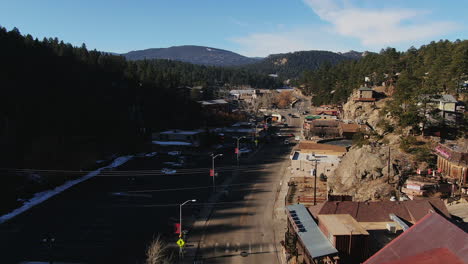 Aerial-Cinematic-drone-fly-over-Downtown-Evergreen-and-ice-skating-lake-in-Colorado-cars-driving-through-town-forward-movement-mid-winter-no-snow