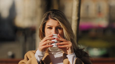 Caucasian-attractive-blonde-woman-drinking-coffee-in-slow-motion-looking-and-smiling-to-camera