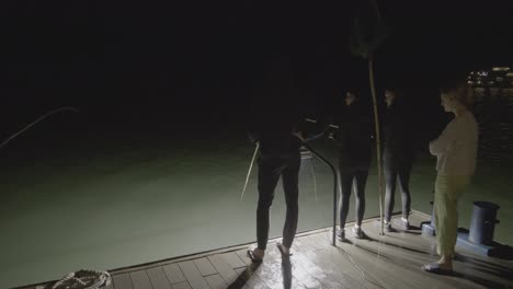 Un-Grupo-De-Personas-Pescando-Calamares-En-La-Popa-De-Un-Barco-Turístico-En-La-Bahía-De-Ha-Long,-Vietnam,-Por-La-Noche.