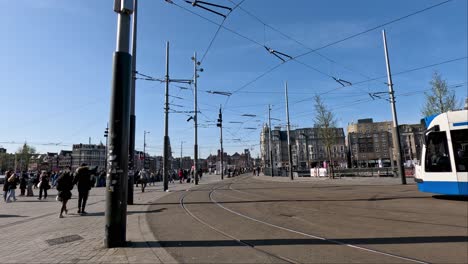 Blick-Auf-Die-Oberleitungen-Der-Straßenbahn-Vor-Dem-Amsterdamer-Hauptbahnhof-Mit-Vorbeigehenden-Menschen