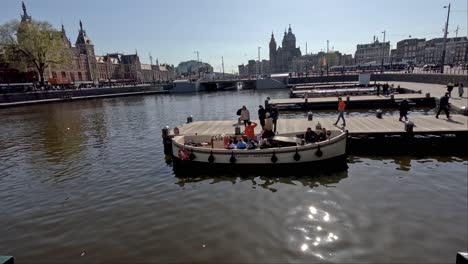 Tourists-Boarding-Small-Tour-Boat-Beside-Pier-In-Amsterdam-On-Sunny-Day