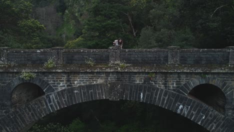 Drone-view-of-woman-standing-on-old-bridge-in-Madeira,-Portugal