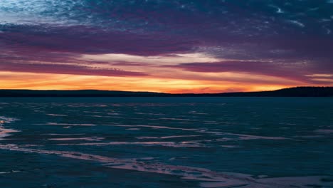 Dramatic-sunset-timelapse-at-an-icy-lake,-sunlight-colors-reflecting-on-clouds