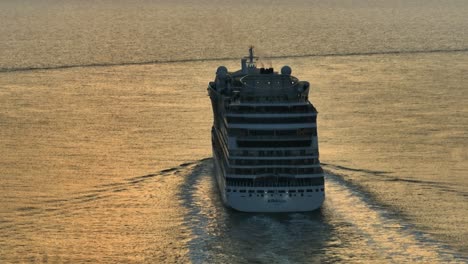 Schwenk-Luftaufnahme-Eines-Kreuzfahrtschiffes,-Das-Bei-Sonnenuntergang-Von-Rotterdam-(Niederlande)-Aus-Aufs-Meer-Hinausfährt,-Wobei-Das-Wasser-Den-Warmen-Goldenen-Schein-Der-Sonne-Reflektiert