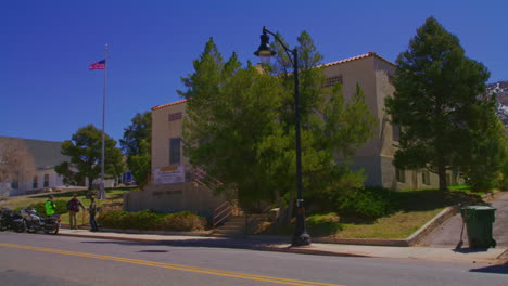 Bandera-Americana-De-Pie-Fuera-Del-Edificio-Con-Fachada-Cubierta-Por-árboles-En-La-Ciudad-De-Eureka-En-El-Condado-De-Juab,-Utah