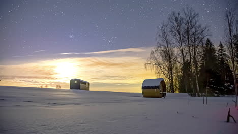 Timelapse-of-bright-moon-and-starry-sky-moving-over-snowy-Nordic-landscape-with-barrel-sauna-and-cabin-hut