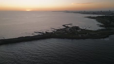 Cinematic-Aerial-Panorama-of-Punta-Carretas-Uruguayan-Peninsula-at-Sunset-Land-Formation-Across-Calming-Ocean-Waters