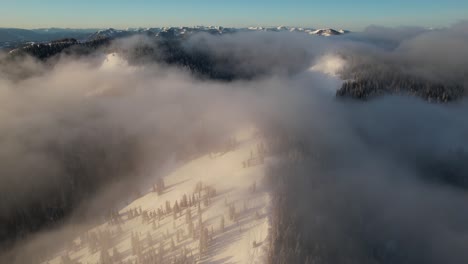 Luftaufnahme-Eines-Sonnigen-Wintermorgens,-Der-über-Schneebedeckte-Hügellandschaften-Und-Wolken-Fliegt