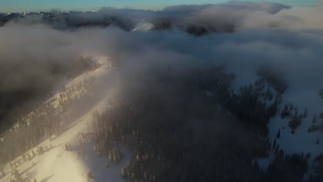 Aerial-View-of-Pristine-Mountain-Landscape-on-Winter-Morning,-Flying-Above-Light-Clouds-and-Pine-Forest