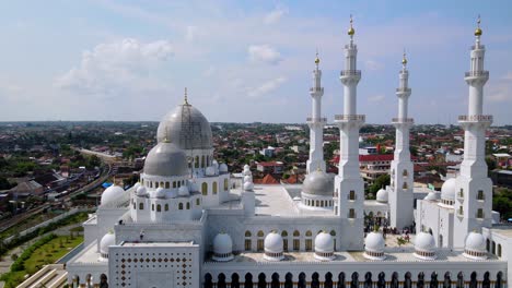 Aerial-view-of-big-white-mosque-with-cupola-and-minarets-against-cloudy-blue-sky