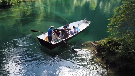 Turistas-Multiétnicos-Disfrutando-De-Un-Paseo-En-Bote-Con-Fondo-De-Cristal-Observando-Peces-En-Aguas-Cristalinas-De-Color-Turquesa-Del-Famoso-Lago-Alpino-Blausee-En-Kandergrund,-Suiza