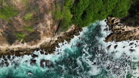 Aerial-view-of-waves-hitting-rocks-on-the-coast-of-Puerto-Escondido,-Mexico---overhead,-drone-shot