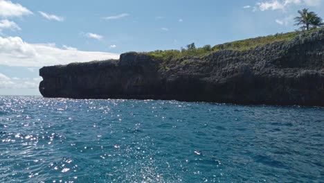 Sparkling-surface-sea-with-rocky-cliff-seen-from-boat,-Playa-Fronton-beach-in-Samana-Peninsula,-Dominican-Republic