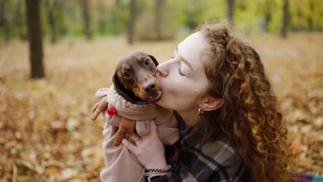 Curly-woman-hold-stylish-dachshund-and-kissing.-Autumn-outdoor-portrait