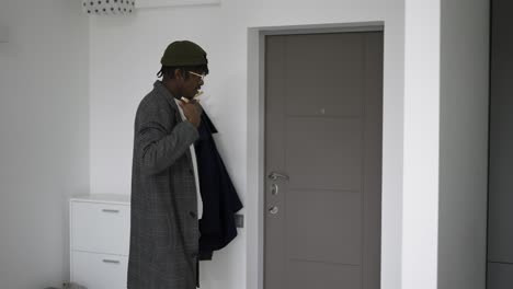 Black-man-in-front-home-door-putting-on-trendy-coat,-leaving-house,-slow-motion
