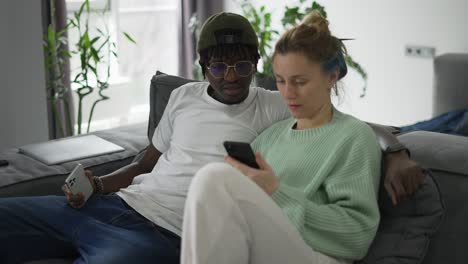Happy-biracial-couple-relaxing-on-sofa-with-smartphone