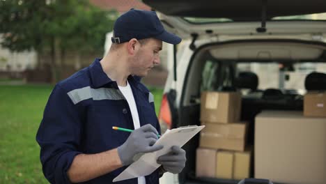 Young-delivery-man-checking-delivery-list.-Delivery-man-in-cap-and-documentation-in-hands-outdoor.-Courier-with-parcel.-Male
