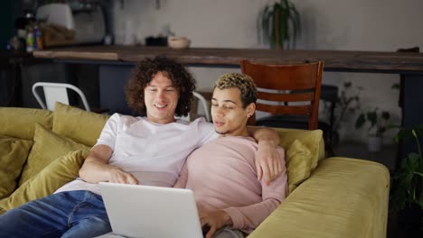 Hübsches-Schwules-Paar,-Das-Einen-Laptop-Benutzt,-Während-Es-In-Einem-Wohnzimmer-In-Einer-Gemütlichen,-Stilvollen-Wohnung-Sitzt