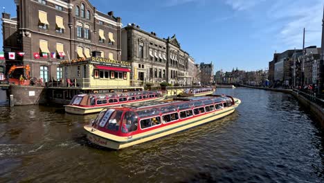 Canal-Cruise-Boats-Going-Past-Rondvaart-Koou-station-at-Oude-Turfmarkt-In-Amsterdam
