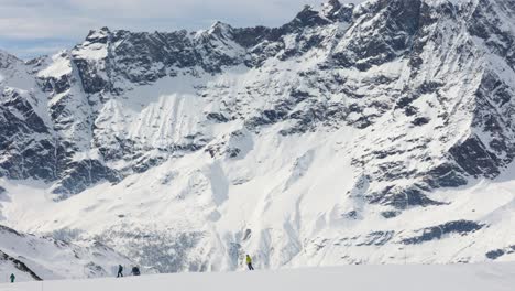 Skiers-ski-on-slope-in-Cervinia-ski-resort-with-massive-mountain-range-peak-in-background