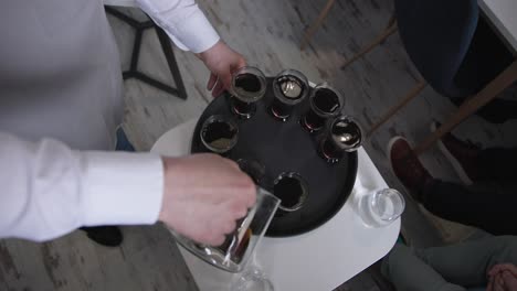 Professional-barista-pours-dark-coffee-into-glass-cups-on-spinning-tray
