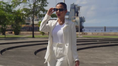 A-young-woman,-donning-a-business-suit,-stands-amidst-the-vibrant-cityscape-with-her-sunglasses-in-hand